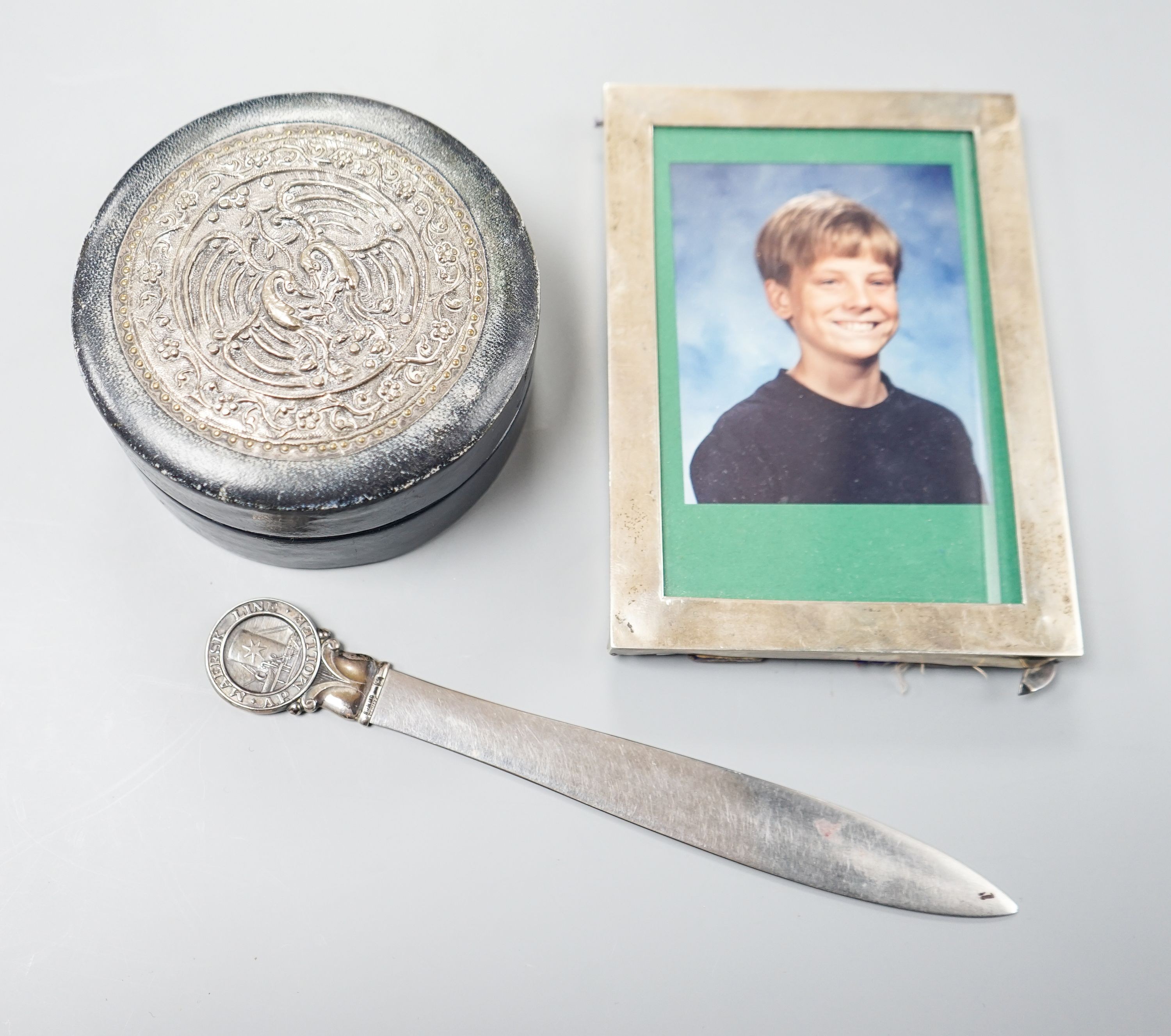 An Edwardian silver mounted photograph frame, 15.5cm, a letter opener with white metal finial and blue leather stud box with Far Eastern embossed white metal panel to lid.